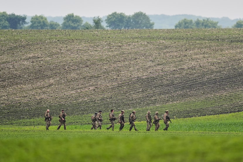 Members of law enforcement agencies walk through a field near a vehicle suspected to belong...