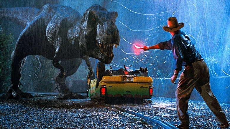 Dr. Grant waves a flare in front of a T-Rex in the rain in Jurassic Park