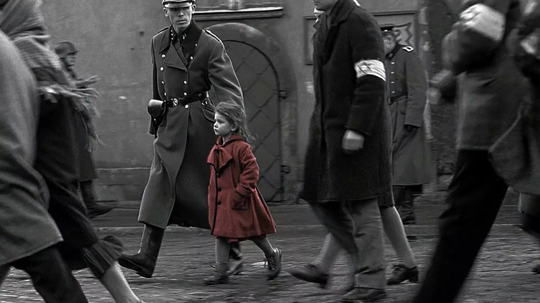 The little girl in a red dress walking next to a Nazi in Schindler