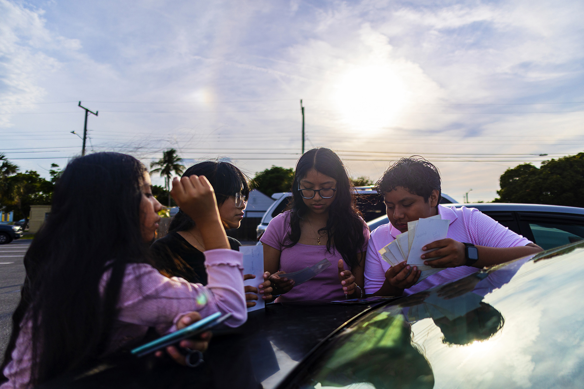 Two women and two teenagers look at family photos on top of a car trunk.