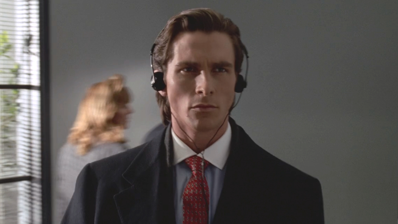 A serious looking Christian Bale wears headphones as he walks down a hallway in American Psycho.