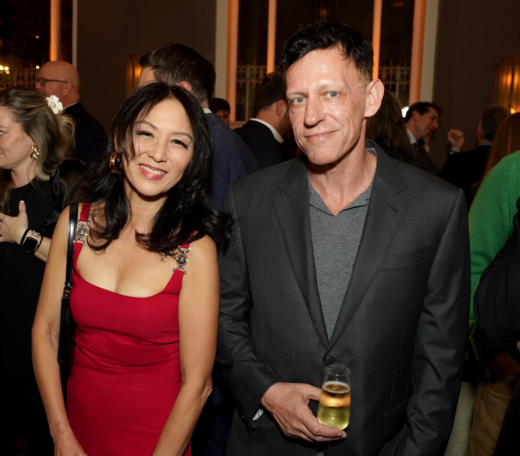 a woman in a red dress and a man in a suit holding champagne at a party pose for a photo