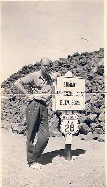 Archival photo of Julius leaning against a sign marking the summit of Mt. McKenzie.