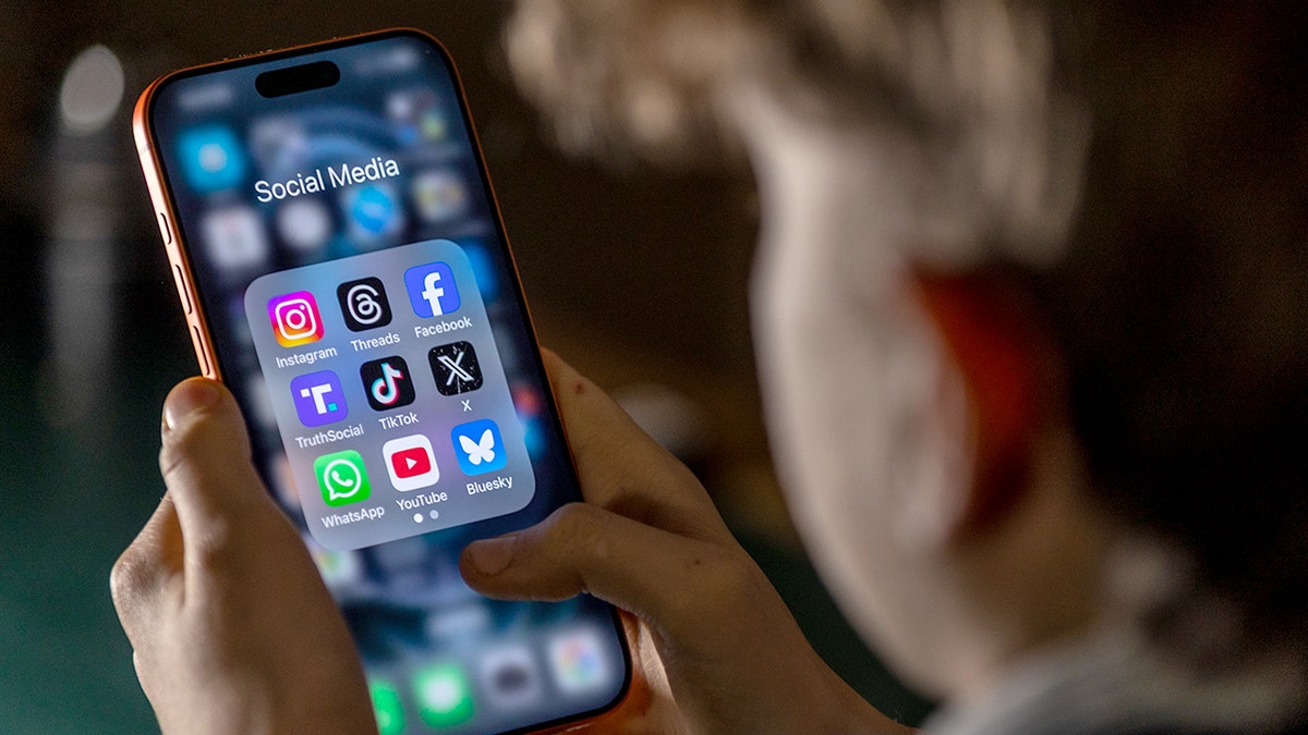 A teen holding a phone displaying nine social media app icons on the screen.