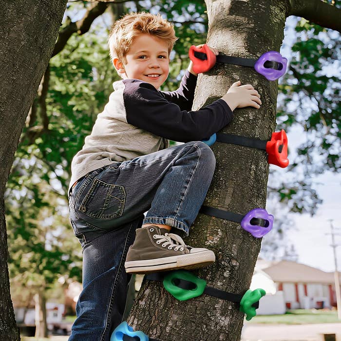 Child smiling, climbing a tree with colorful handholds, wearing casual jeans and sneakers