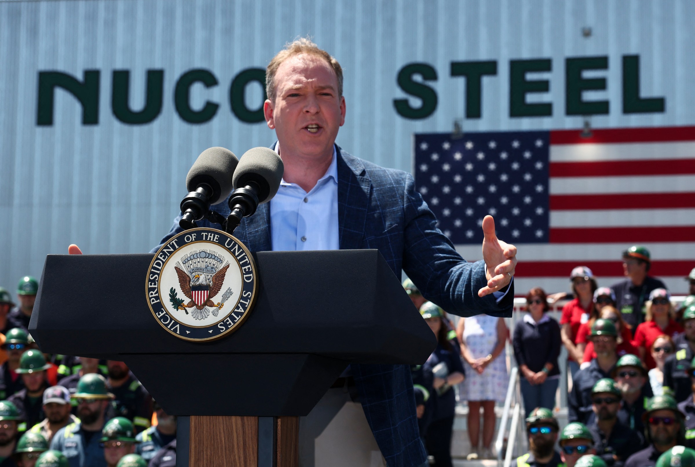 EPA administrator Lee Zeldin stands in front of a Nucor Steel building with an American flag in the background.
