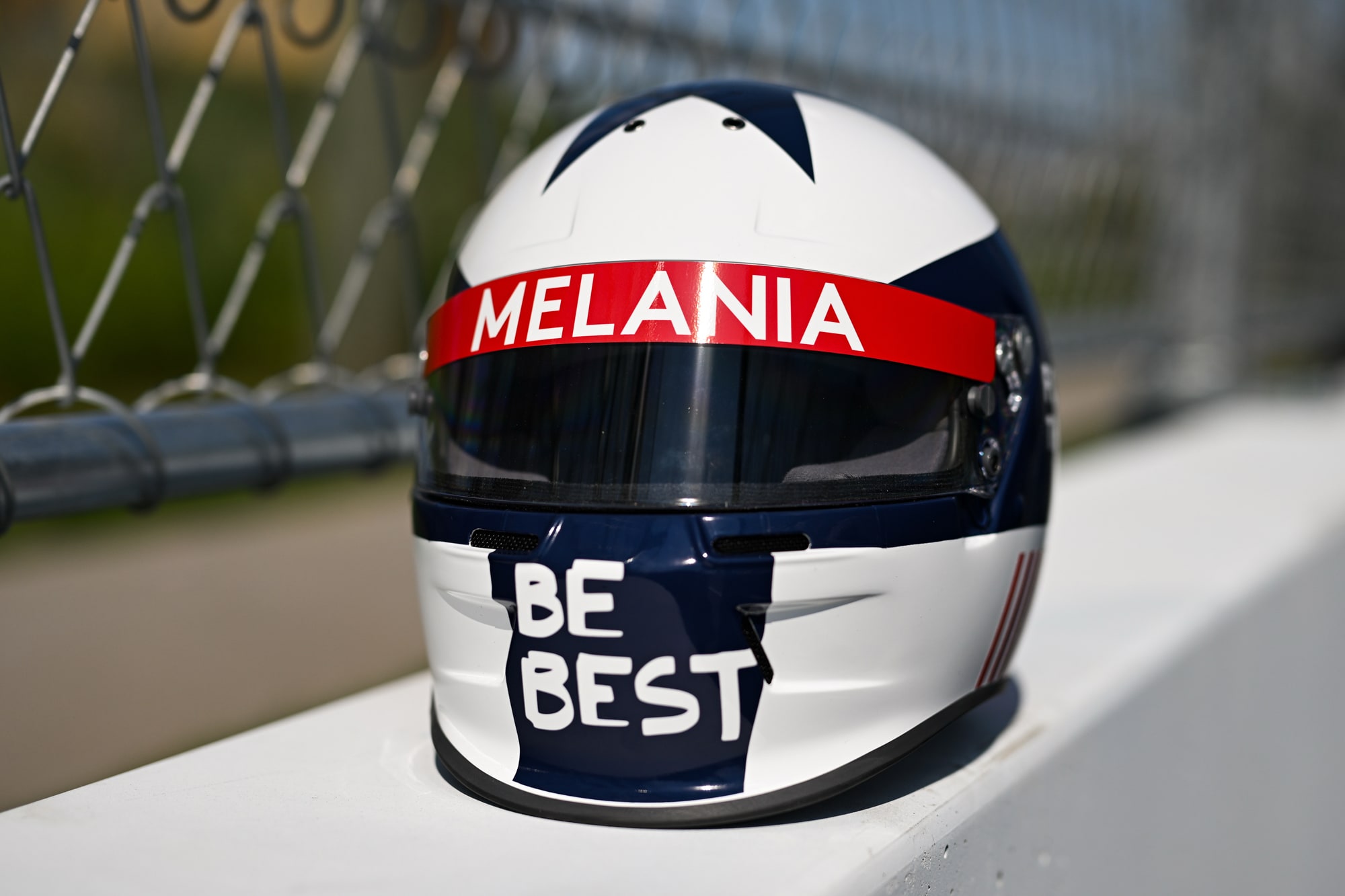 The front side of a red, white, and blue racing helmet with text that reads: "Melania" and "Be Best"