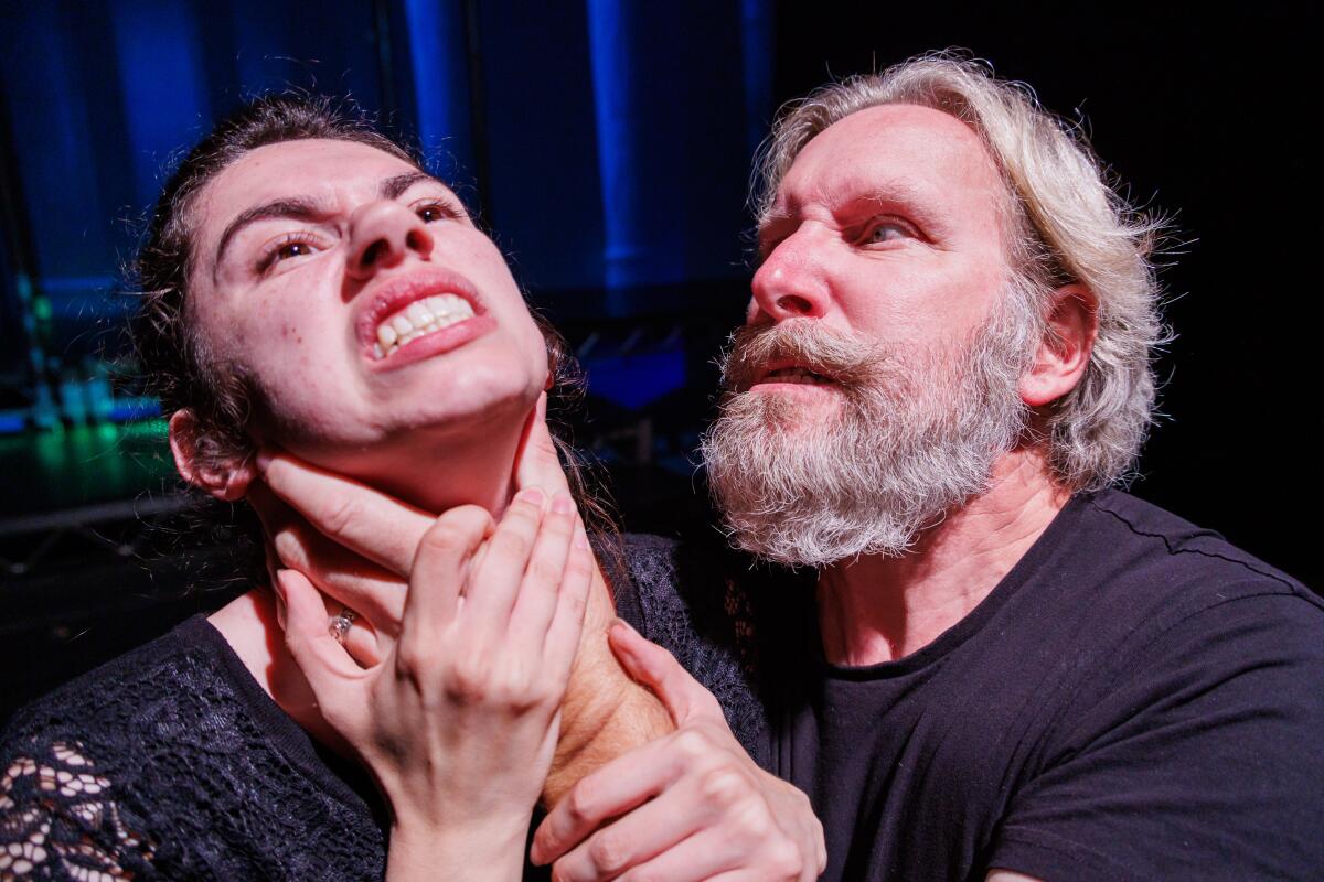 A male actor grips a female actor by the throat.